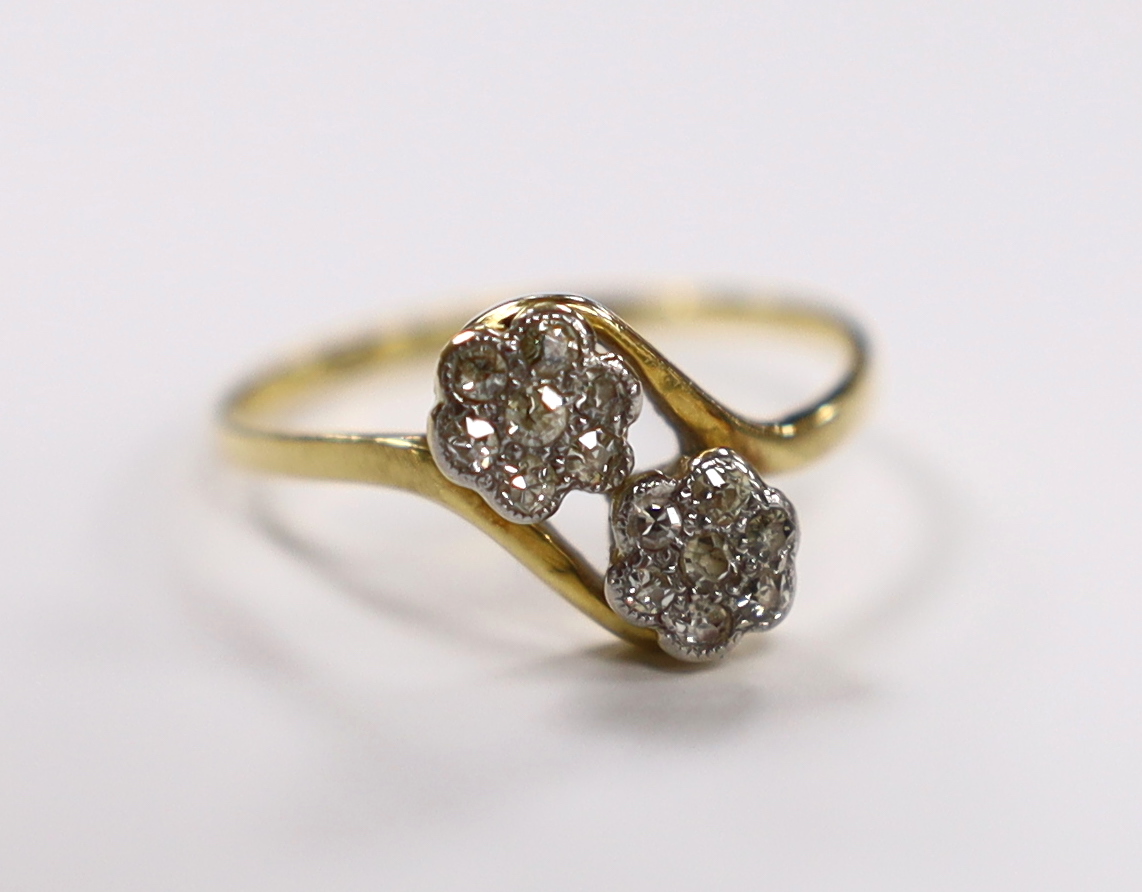 A yellow metal and diamond cluster set double flower head crossover ring, size N/O, gross weight 2 grams.